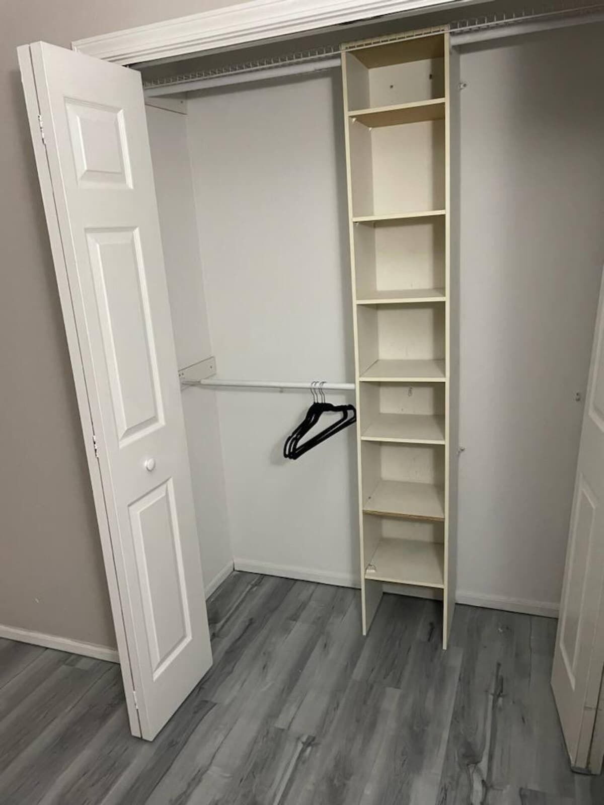Un dressing avec des murs blancs, un plancher en bois et une tringle en métal pour suspendre les vêtements.