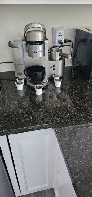 Une cuisine équipée d’une machine à café Keurig, d’une cafetière et de plusieurs dosettes de café posées sur le comptoir.