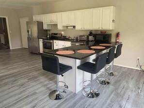 Une cuisine dotée d’un îlot central, de meubles blancs, d’appareils électroménagers en acier inoxydable et de tabourets de bar noirs.