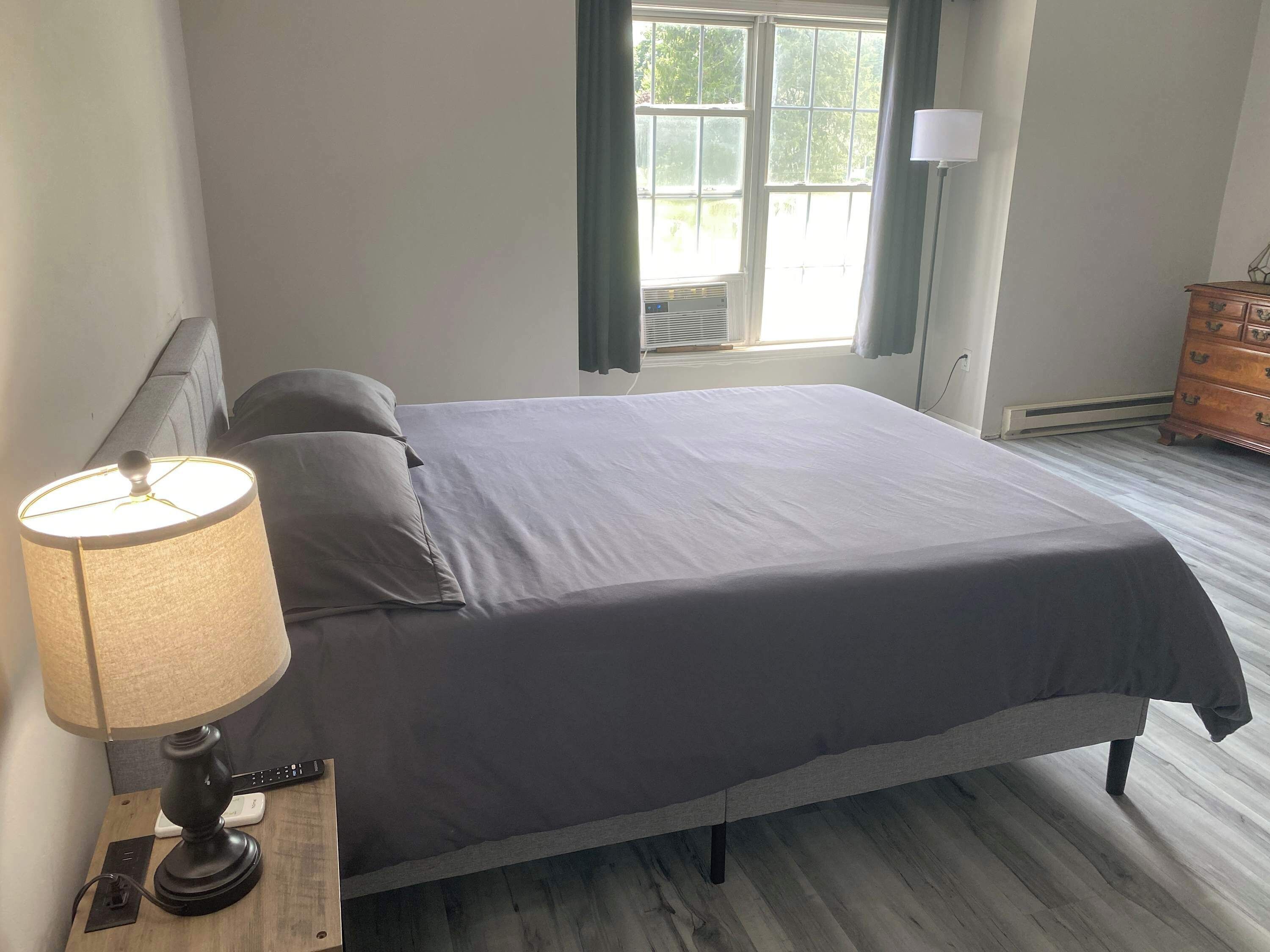 Een slaapkamer met een bed, een bedlampje, een kaptafel en een raam met gordijnen.