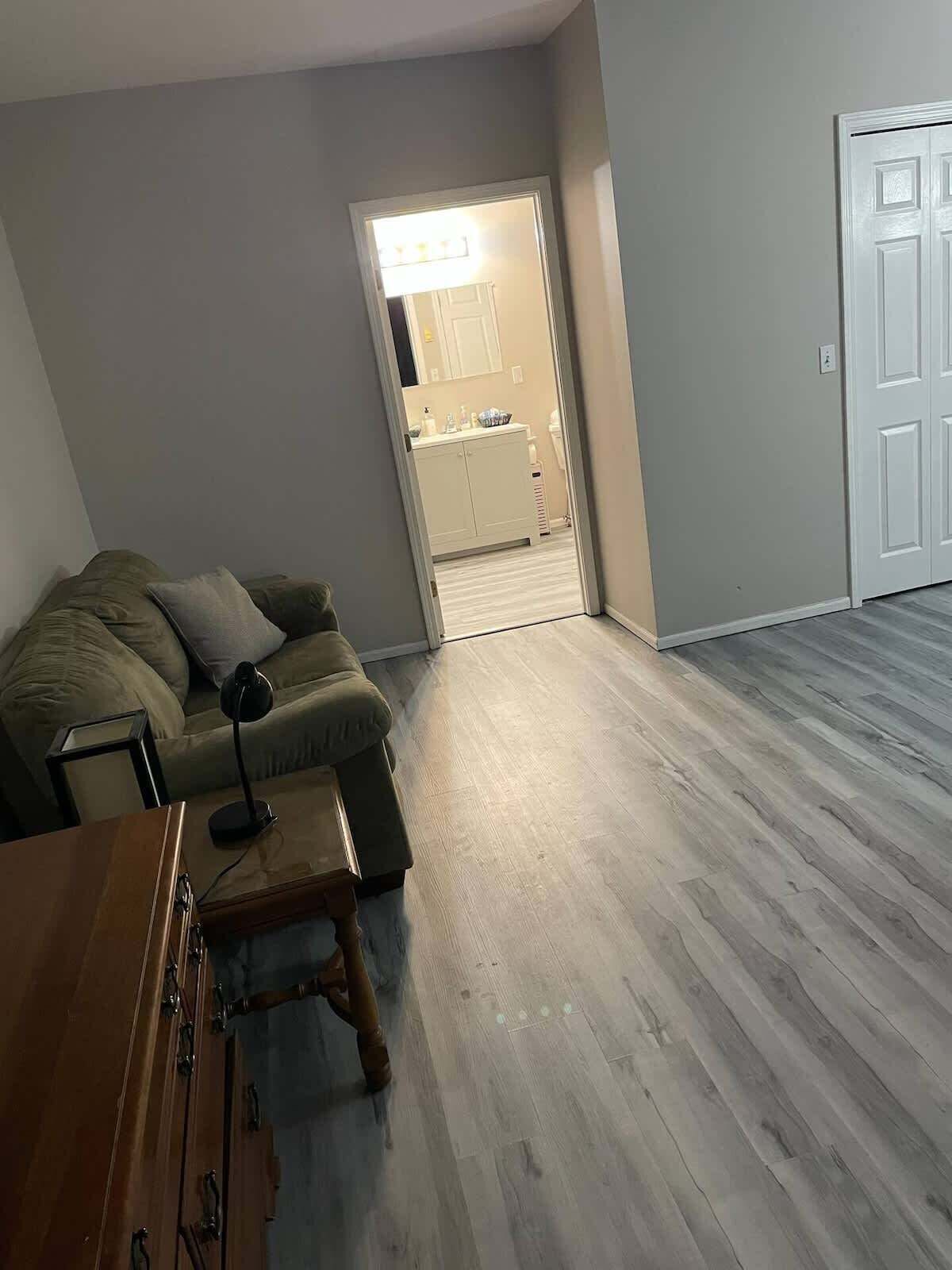 A living room with a sofa, a wooden side table, and a door leading to a bathroom.