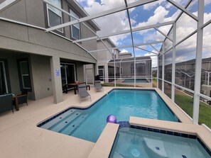 Ein Schwimmbad mit Glasüberdachung, eine Terrasse mit Sitzgelegenheiten und Blick auf angrenzende Häuser.