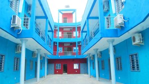 A multi-story building with a central courtyard, featuring a symmetrical design with blue and red walls, and multiple air conditioning units. - Residence MaryHouse (Cotonou)