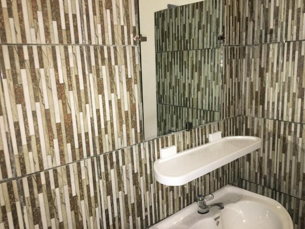 Ett badrum med modern design, med en vägg som har ett marmormönster och ett handfat som är inbyggt bakom glas.