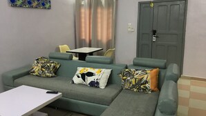 A modern living room with a sectional sofa, a small table, and a grey door. - Residence MaryHouse (Cotonou)