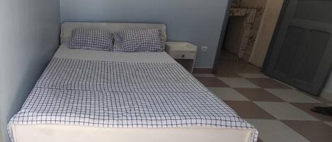 Una cama individual con colcha a cuadros, una mesita de noche y una ventana con vistas a una zona empavedada.