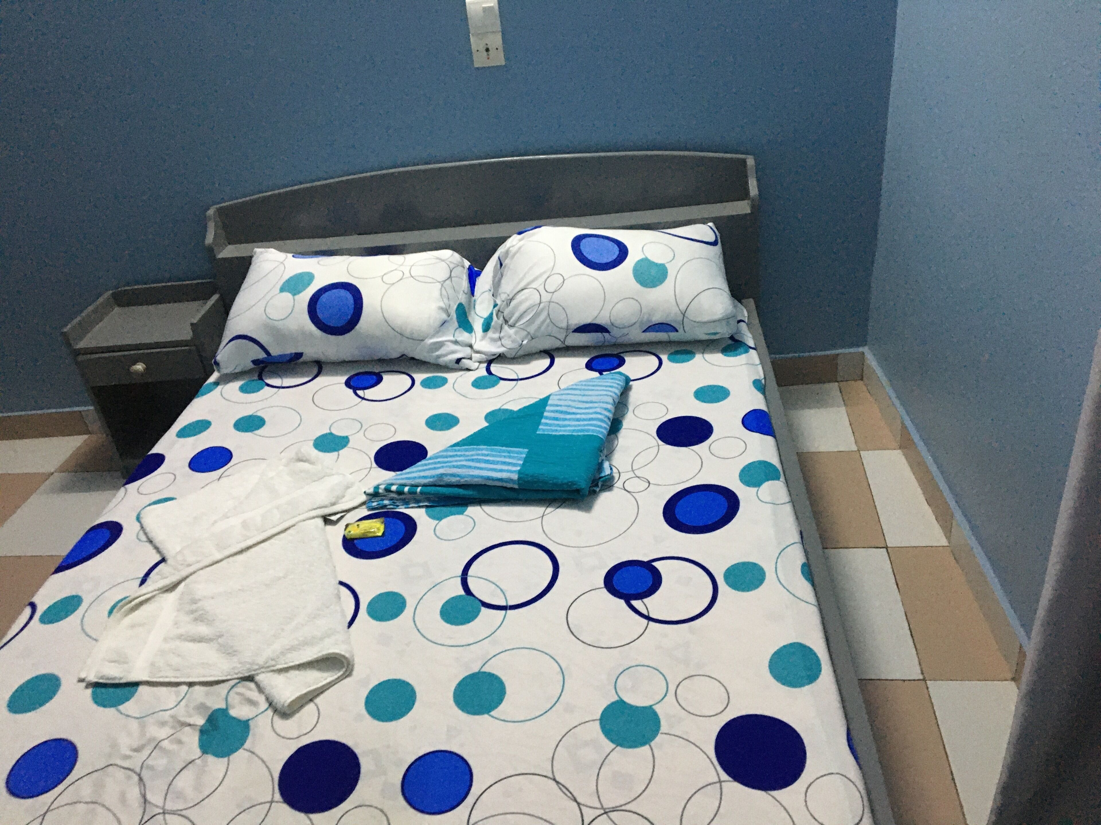 A bed with a polka dot bedspread, a pillow, a folded towel, and a nightstand.
