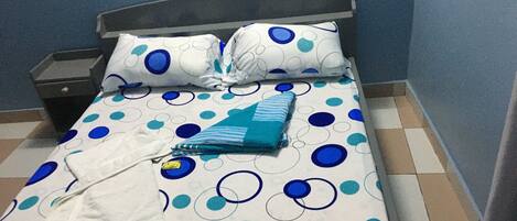 A bed with a polka dot bedspread, a pillow, a folded towel, and a nightstand.