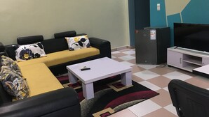 A living room with a sofa, a coffee table, a TV, and a refrigerator. - Residence MaryHouse (Cotonou)