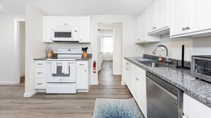 A modern kitchen with white cabinets, a built-in oven, a microwave, a dishwasher, and granite countertops. - *Mins to the Beach | Portsmouth | Maine* (North Hampton)