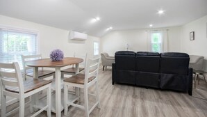 A modern, well-lit room with a dining table, chairs, a black sofa, and a window with blinds. - *Mins to the Beach | Portsmouth | Maine* (North Hampton)