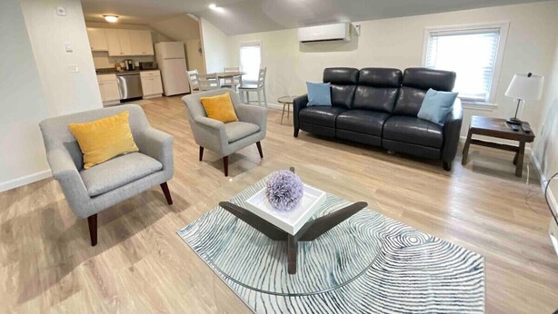 A modern living room with a grey armchair, a black leather sofa, and a patterned rug. - *Mins to the Beach | Portsmouth | Maine* (North Hampton)