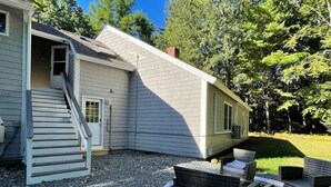 A house with a staircase leading to a door, a small outdoor seating area with wicker furniture, and a gravel driveway. - *Mins to the Beach | Portsmouth | Maine* (North Hampton)