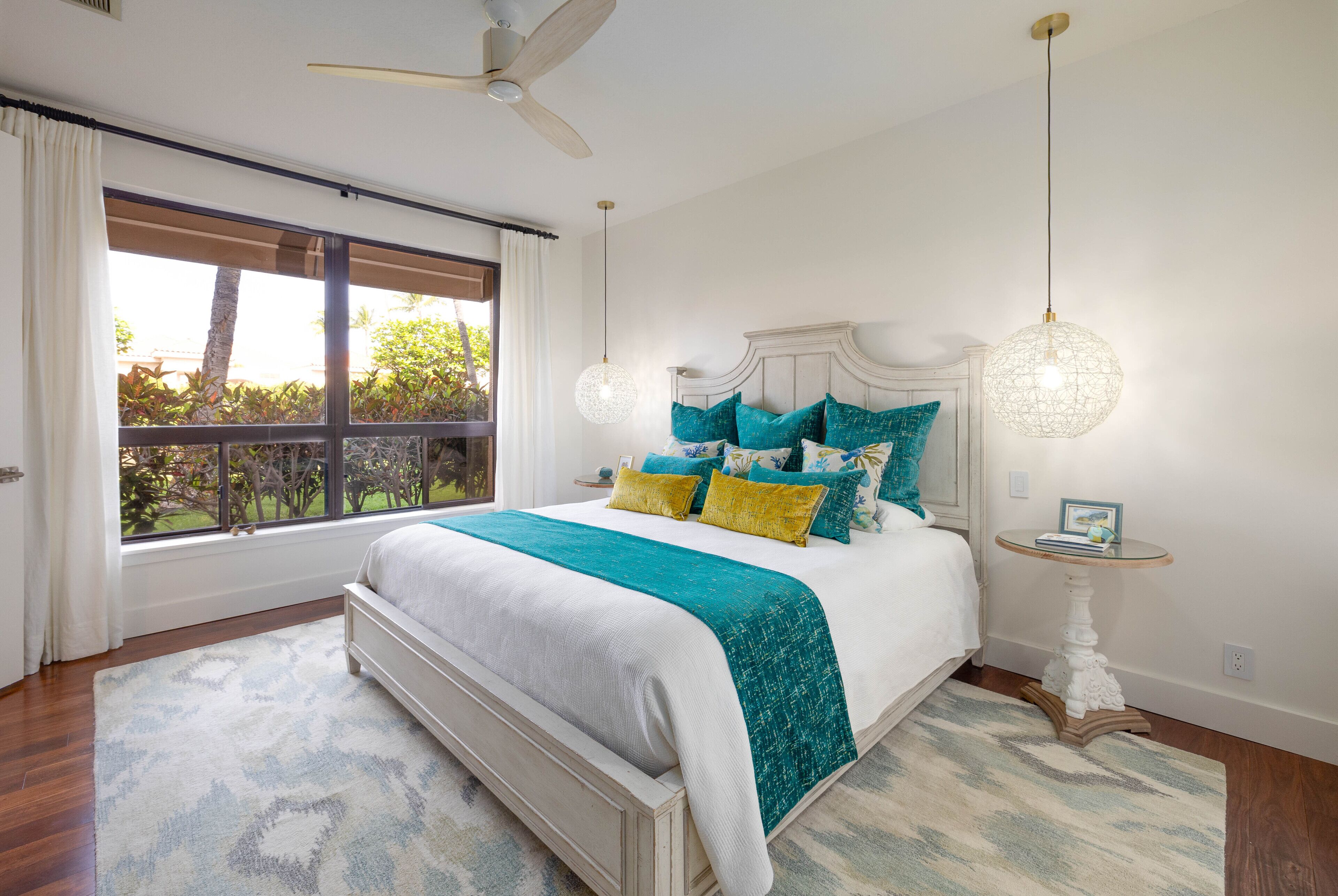 Quarto com uma cama grande, um ventilador de teto, uma janela com cortinas e uma mesa de cabeceira com abajur.