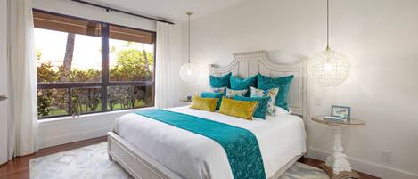 Quarto com uma cama grande, um ventilador de teto, uma janela com cortinas e uma mesa de cabeceira com abajur.
