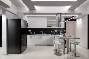 A modern kitchen with a black refrigerator, stainless steel appliances, white cabinets, and a bar area with stools.