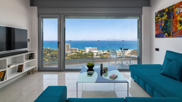 A modern living room with a large TV, a glass coffee table, a sofa, and a view of the sea. - Rhodes Skyline Suite with out Door Jacuzzi Sea View A2 (Rhodes)