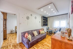Una sala de estar con sofá, una mesa de comedor para cuatro personas y una estantería.