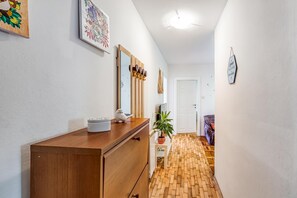 A hallway with a wooden dresser, a mirror, a potted plant, and a door at the end. - Green Hill Zagreb - Apartment Zen, Zagreb, Croatia (Zagreb)