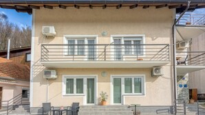A two-story building with a balcony, air conditioning units, and a small outdoor seating area with chairs and a table.