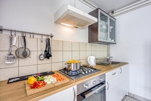 A modern kitchen with a gas stove, a kettle, and a cutting board with vegetables.