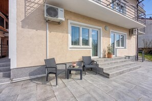 A modern building with a balcony, outdoor seating, and air conditioning units.