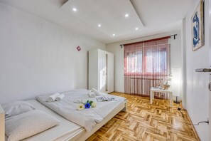 A hotel room with a bed, a bedside table, a window with curtains, and a wooden floor.