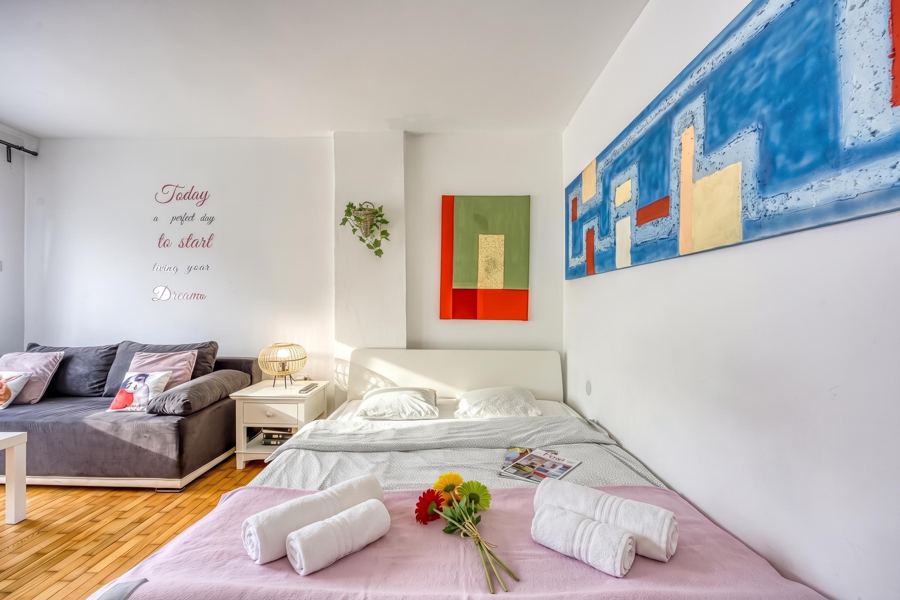 Une chambre moderne comprenant un lit, un canapé, une lampe fixée au mur, une petite table et un mur orné d’un texte motivant.