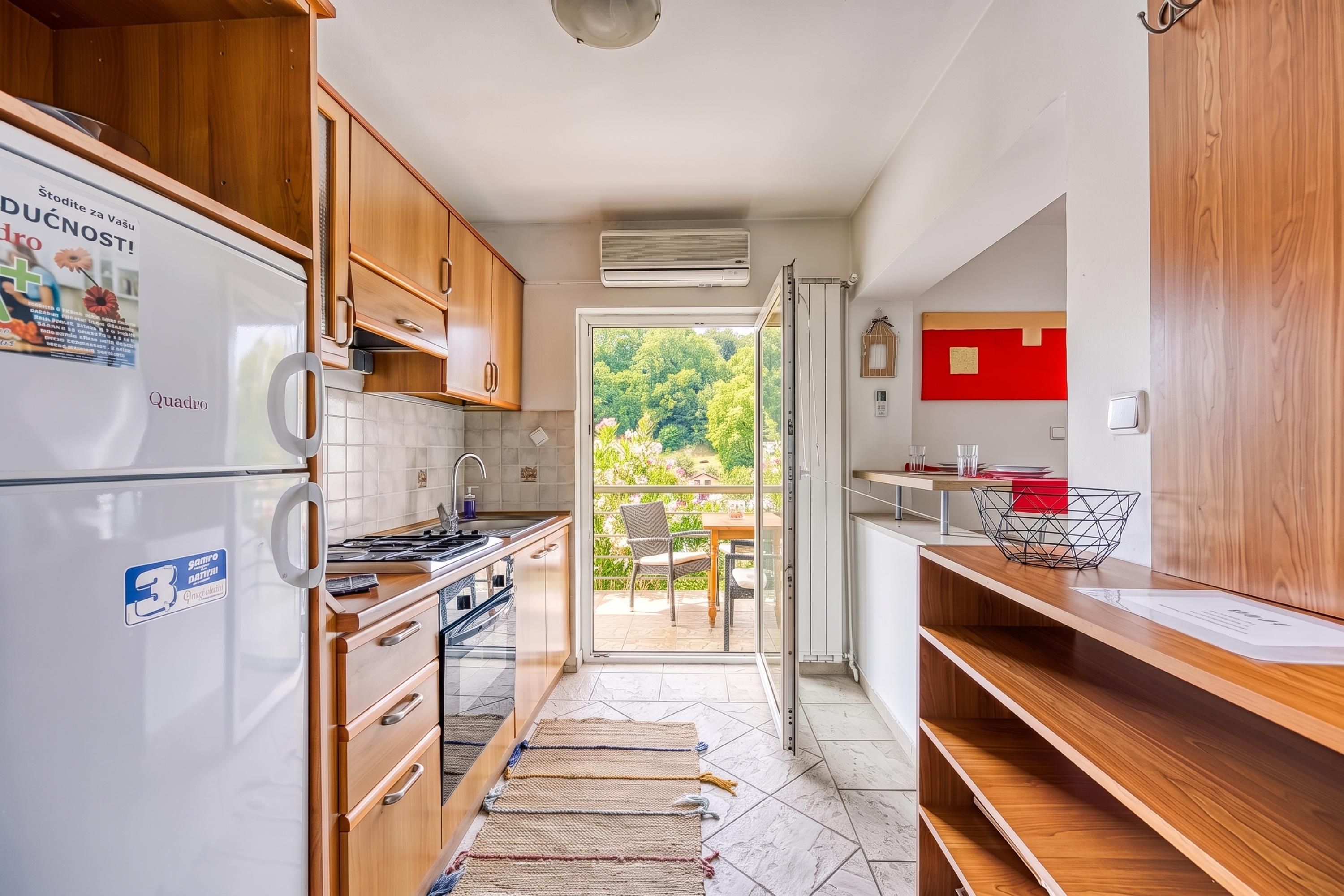 A compact kitchen with wooden cabinets, a built-in stove, and a refrigerator. There is a sliding glass door leading to a patio with outdoor furniture.