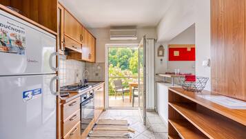 A compact kitchen with wooden cabinets, a built-in stove, and a refrigerator. There is a sliding glass door leading to a patio with outdoor furniture.