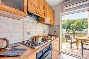Een moderne keuken met houten kastjes, een gasfornuis en uitzicht op een balkon met tuinmeubilair.