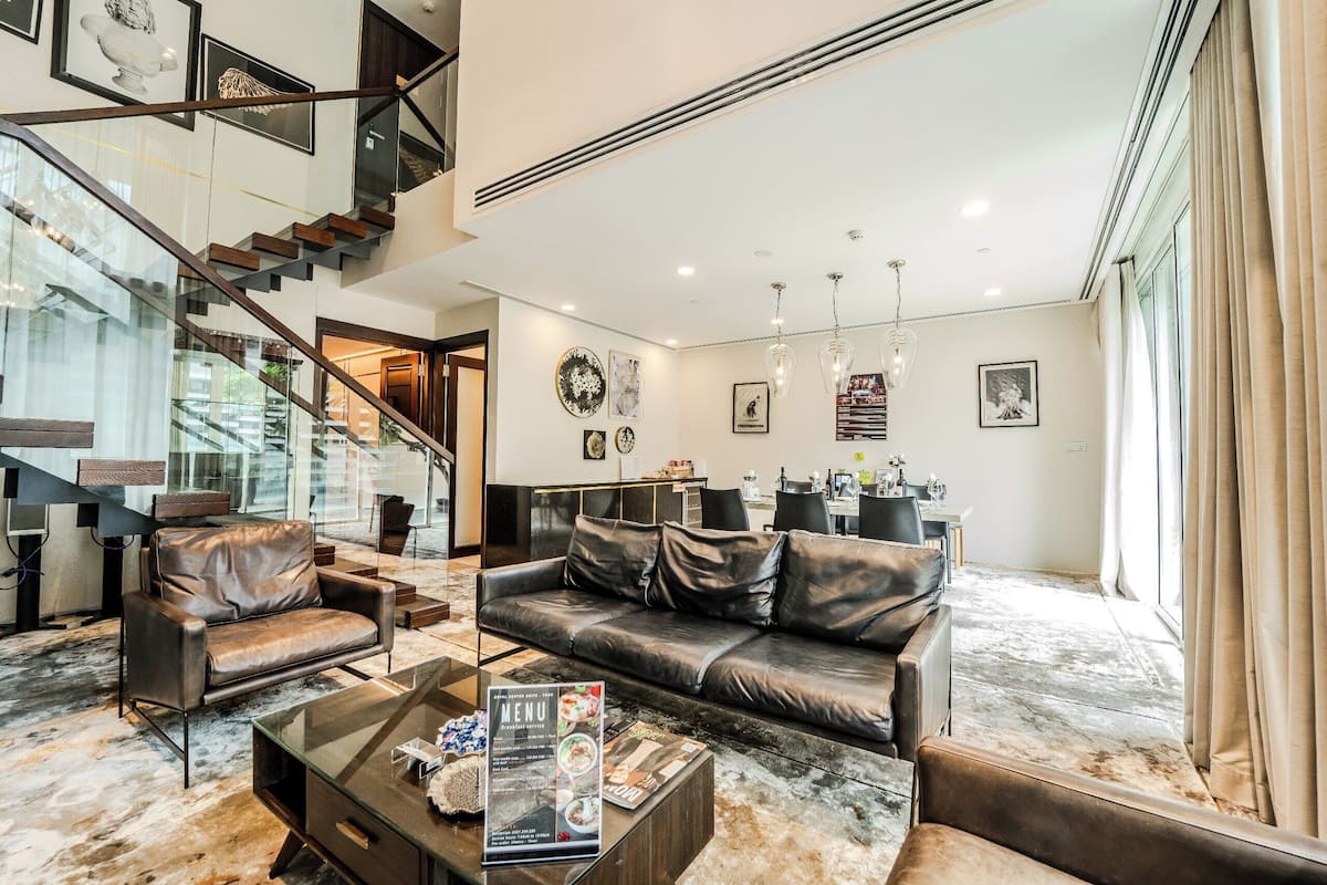 A modern living room with a leather sofa, a coffee table, and a staircase leading to an upper floor.