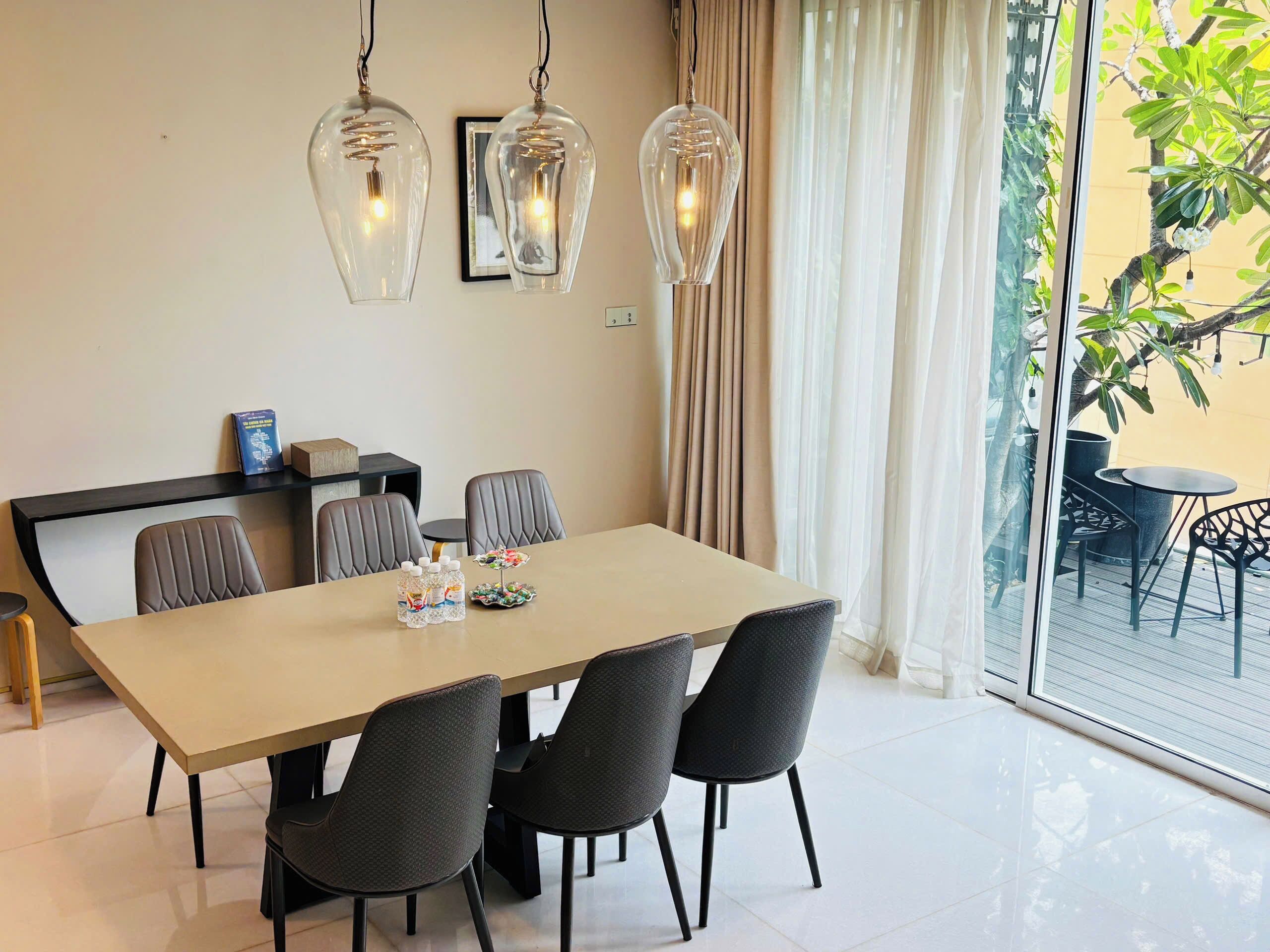 A modern dining area with a long table, six chairs, and two hanging pendant lights.