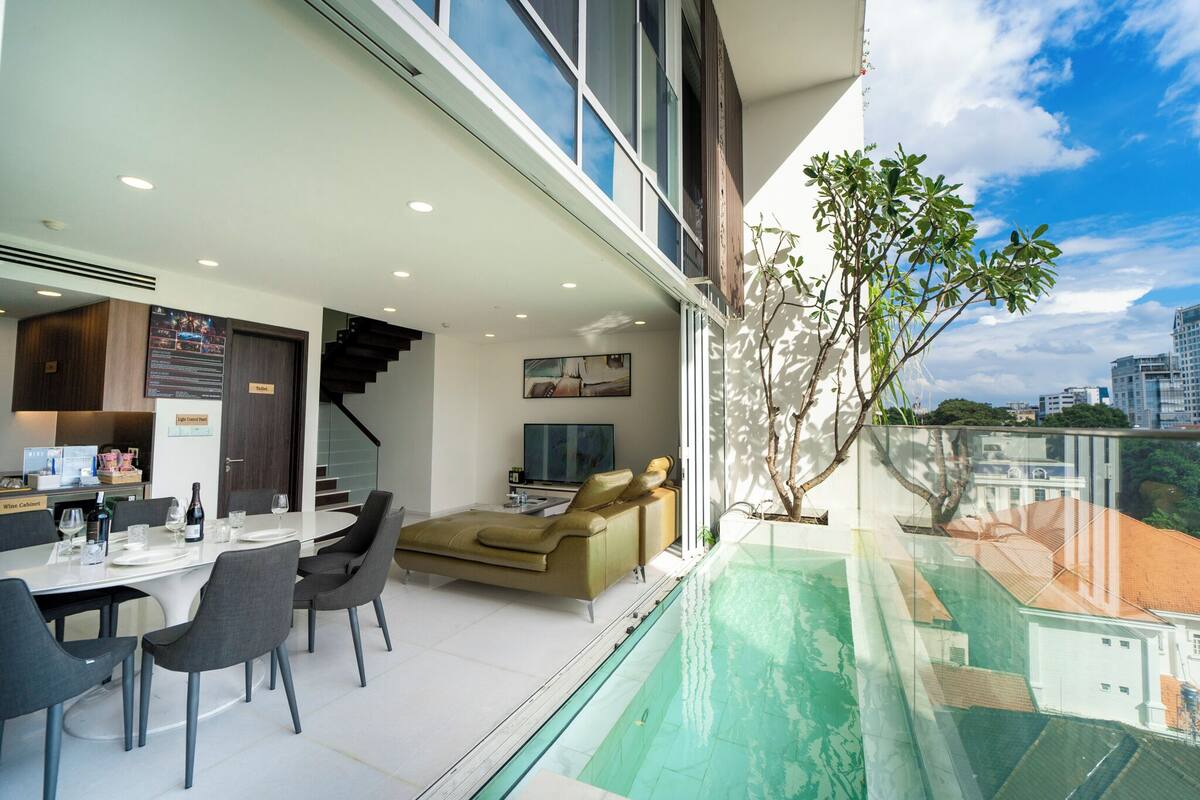 A modern living room with a dining area, a pool, and a staircase leading to an upper floor.