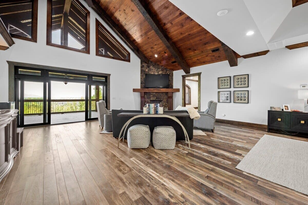 A spacious living room with a fireplace, large windows, and a balcony.