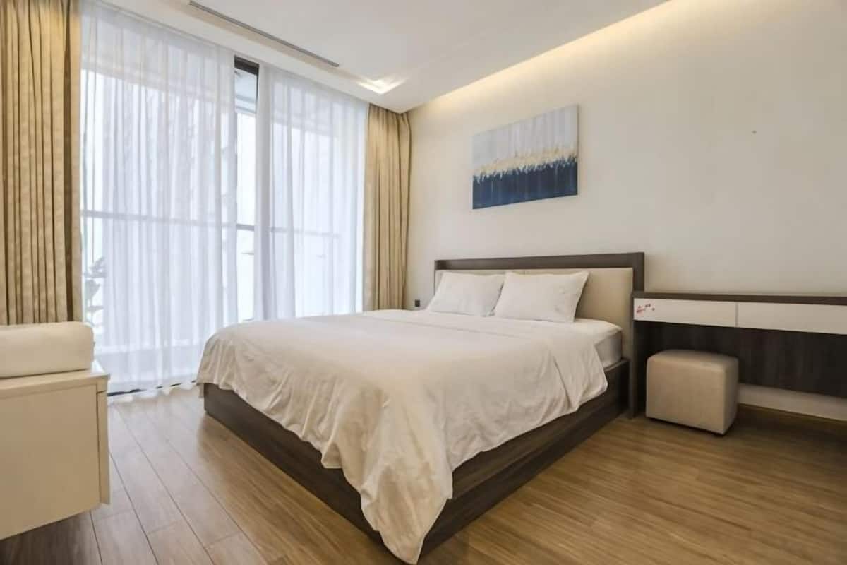 Ein Hotelzimmer mit einem großen Bett, einem Nachttisch, einem Sessel und einem Fenster mit Vorhängen.