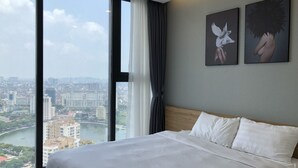 A hotel room with a large bed, a view of a cityscape and river, and two wall art pieces. - Vinhomes Metropolis 3Brs  (Hanoi)