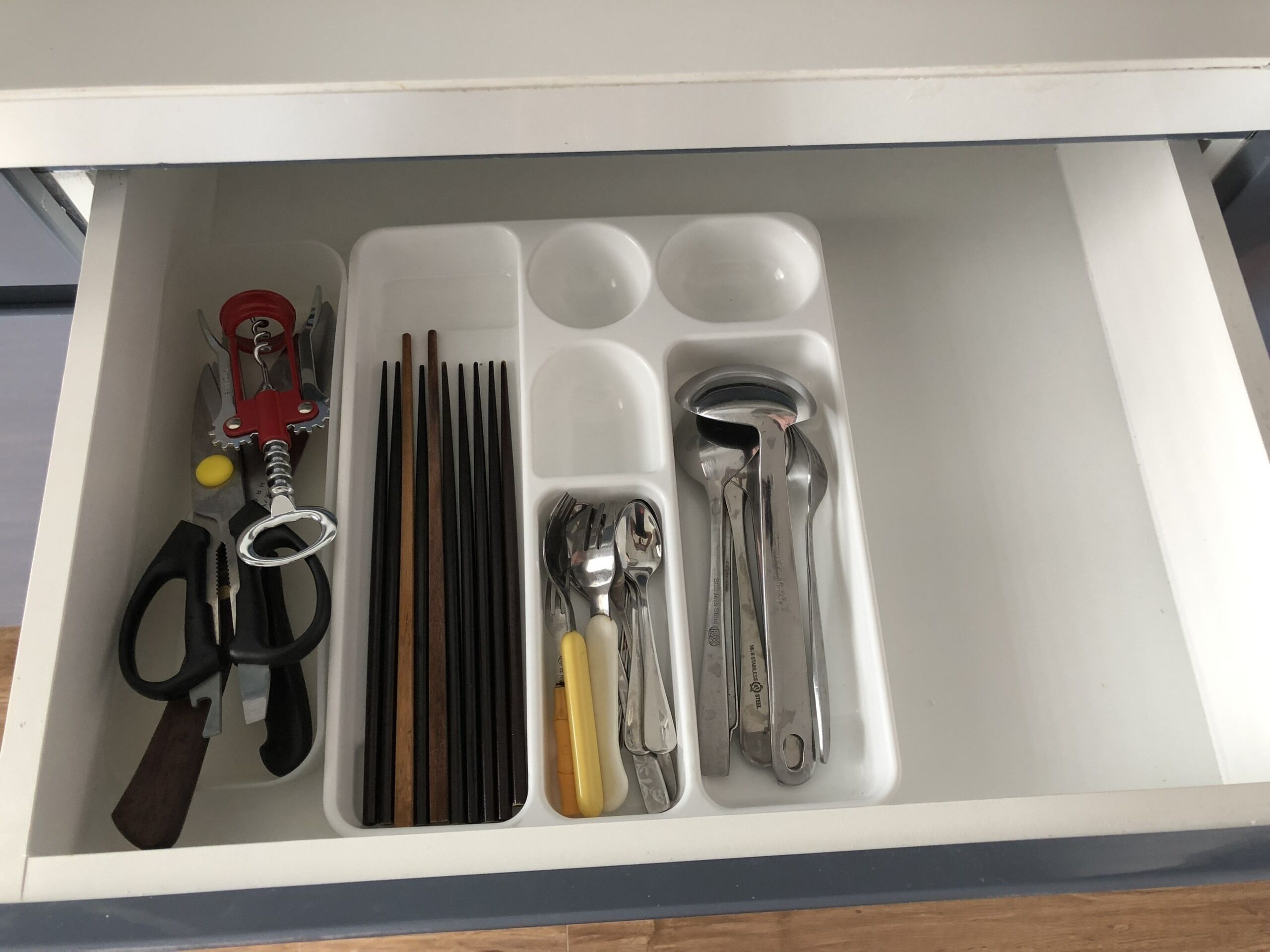 A drawer with compartments containing various kitchen utensils and tools.