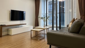 A modern living room with a flat-screen TV, a sofa, a coffee table, and a sliding glass door leading to a balcony. - Vinhomes Metropolis 3Brs  (Hanoi)