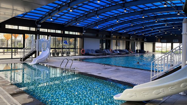 An indoor swimming pool with a glass ceiling, slides, and lounge chairs. - Vinhomes Metropolis 3Brs  (Hanoi)