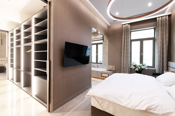 Une chambre moderne avec un grand lit, une armoire intégrée, une télévision et une salle de bain dotée d’une grande fenêtre.