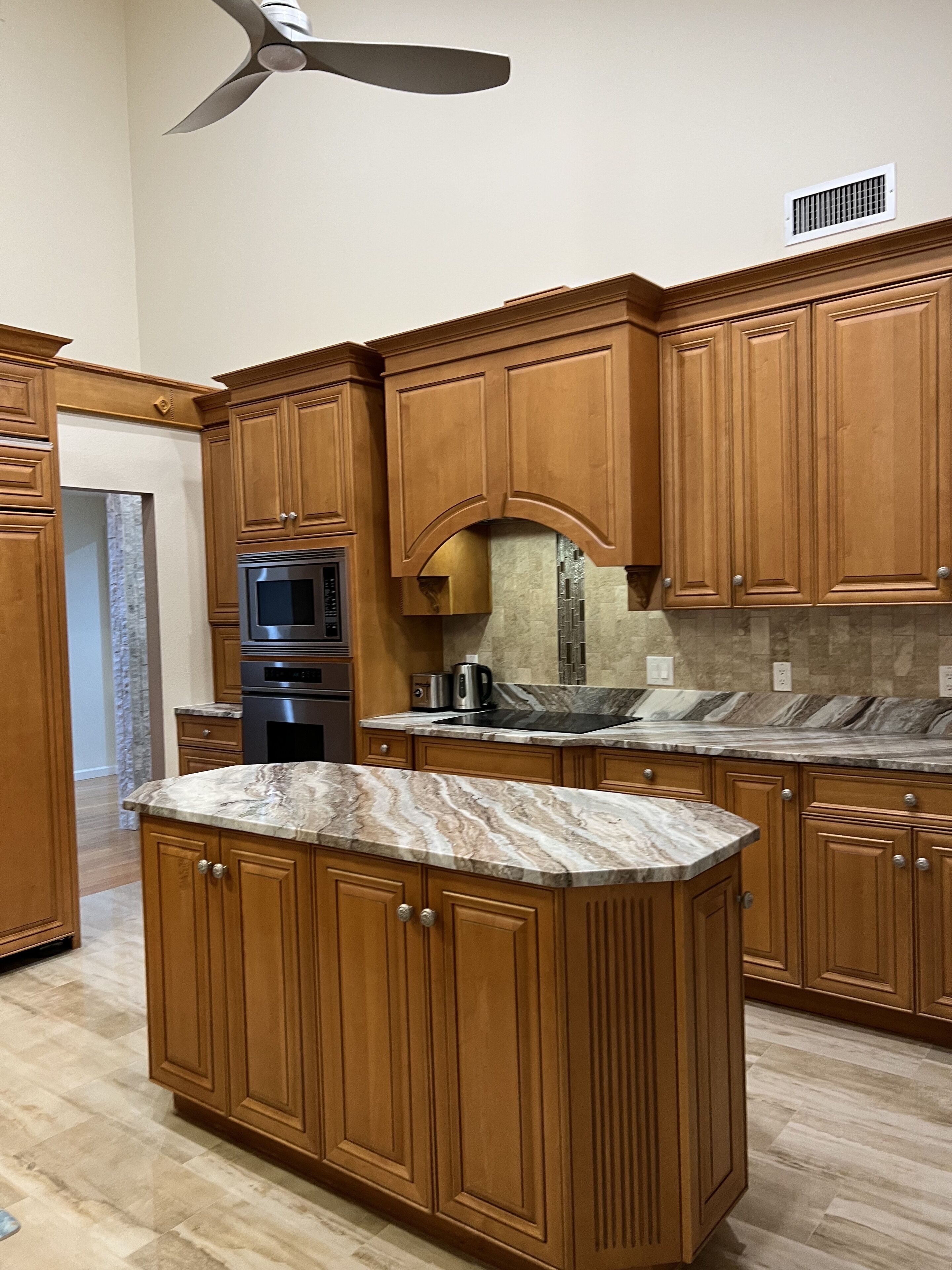 A kitchen with wooden cabinets, a marble countertop, a built-in oven, and a ceiling fan.