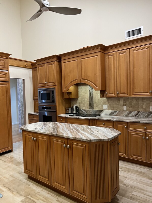 A kitchen with wooden cabinets, a marble countertop, a built-in oven, and a ceiling fan. - Gorgeous house , private road, 0.8 miles to Manasota Beach-RomanticGataway (Englewood)