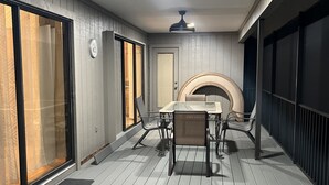 Een overdekte eethoek buiten met een tafel, stoelen, een plafondventilator en een open haard.