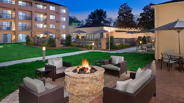 Eine Terrasse mit einem Steinkamin, umgeben von Korbmöbeln, einem Rasen und einem Gebäude mit mehreren Balkonen im Hintergrund.