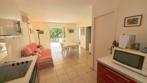 A modern kitchen with a stove, sink, and microwave. There is a dining area with a table and chairs, and a living area with a sofa. - 2-bedroom club villa with large terrace in holiday residence (SIX FOURS LES PLAGES)