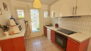 A compact kitchen with white and red cabinetry, a black stove, and a yellow pendant light. - 2-bedroom club villa with large terrace in holiday residence (SIX FOURS LES PLAGES)
