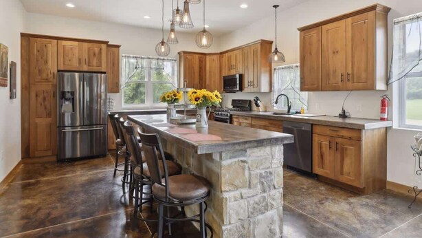 A spacious kitchen with wooden cabinets, a central island with bar stools, a stainless steel refrigerator, and pendant lighting. - Isabelle Creek Haven - Ultimate Group Getaway (Bay City)