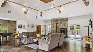 A spacious living room with a stone fireplace, a pool table, and a large gray sectional sofa. - Isabelle Creek Haven - Ultimate Group Getaway (Bay City)