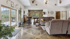 A spacious living room with a stone fireplace, a large sofa, and a dining area with a table and chairs. - Isabelle Creek Haven - Ultimate Group Getaway (Bay City)